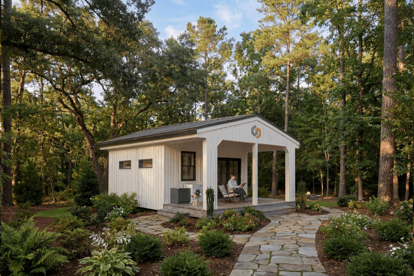 White modern cabins with covered porch, stone pathway, and lush garden setting in wooded landscape
