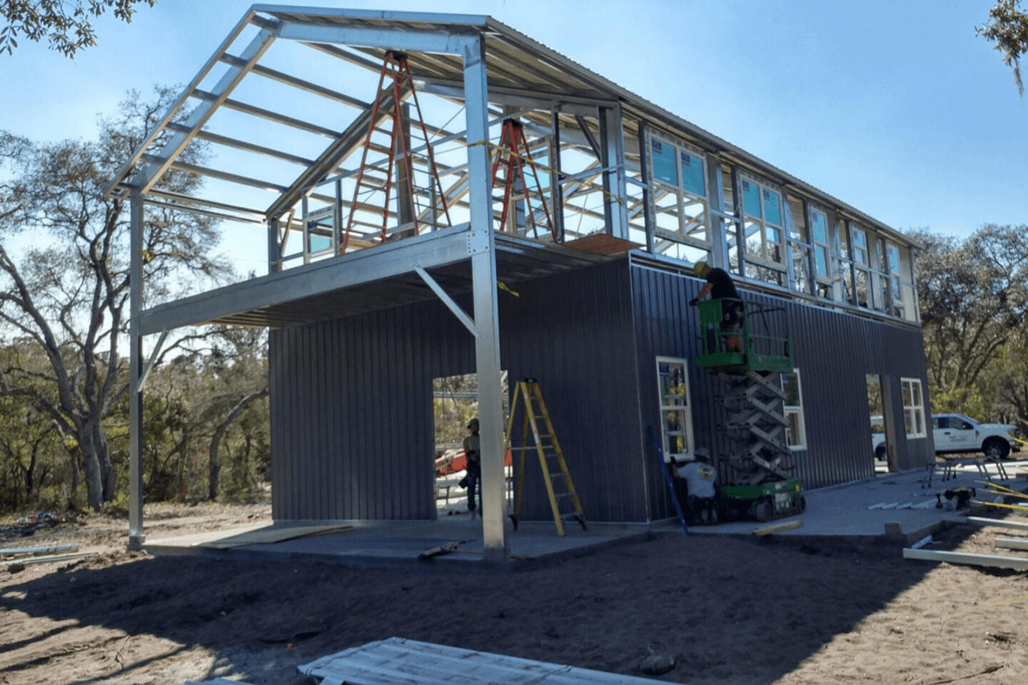 Steel frame construction of two-story steel kit home with glass panels and curved roof structure on red clay site
