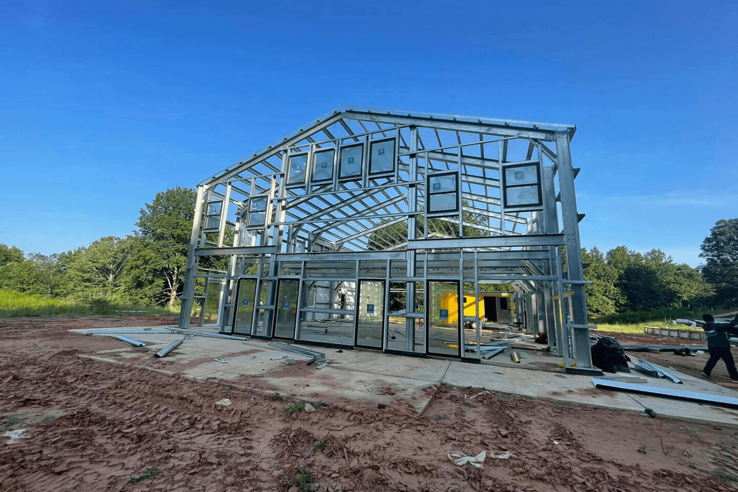 Steel frame construction of two-story steel kit home with glass panels and curved roof structure on red clay site
